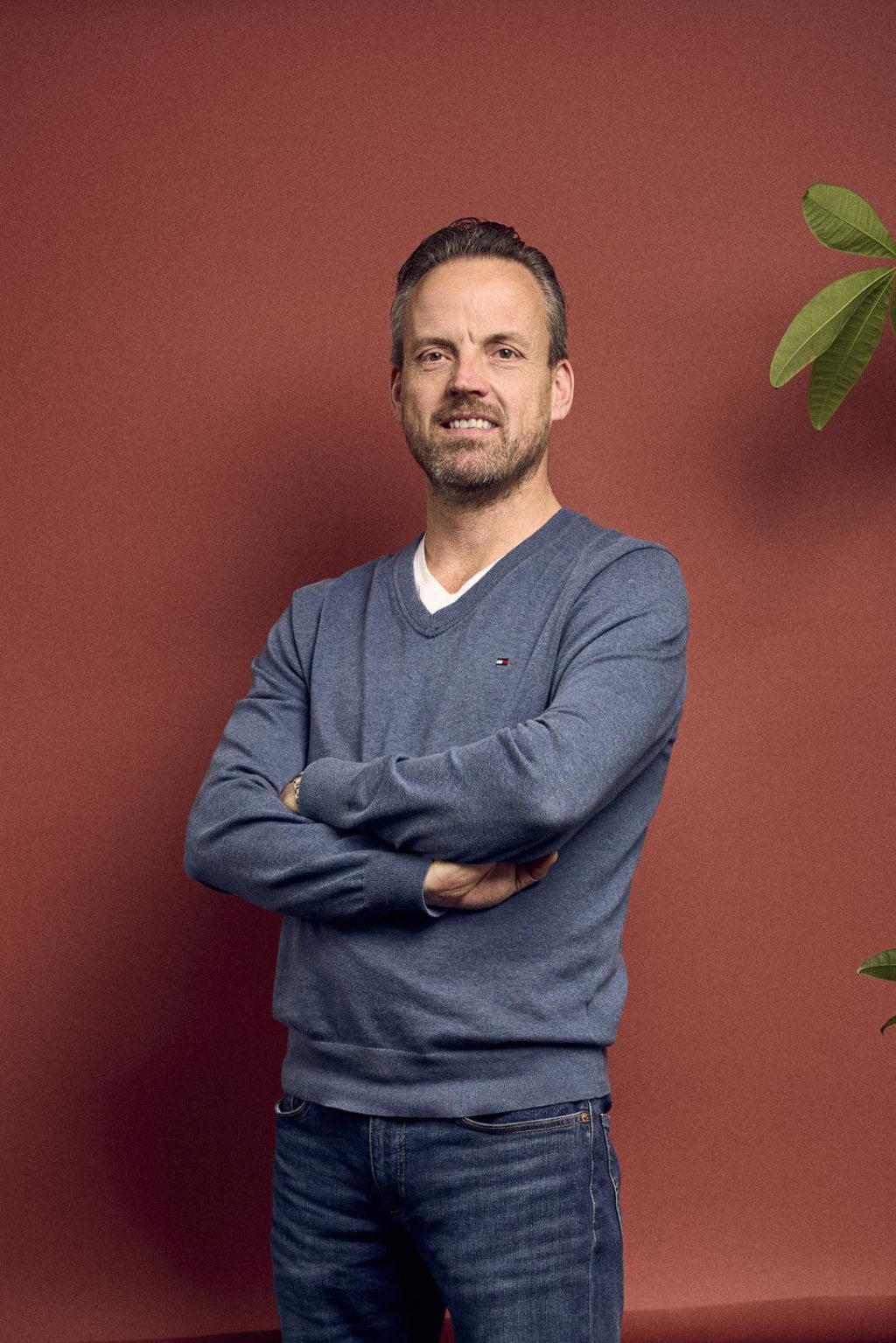 Maarten Heijnen staat voor een rode backdrop in een kantoorruimte met een plant rechts langs hem.