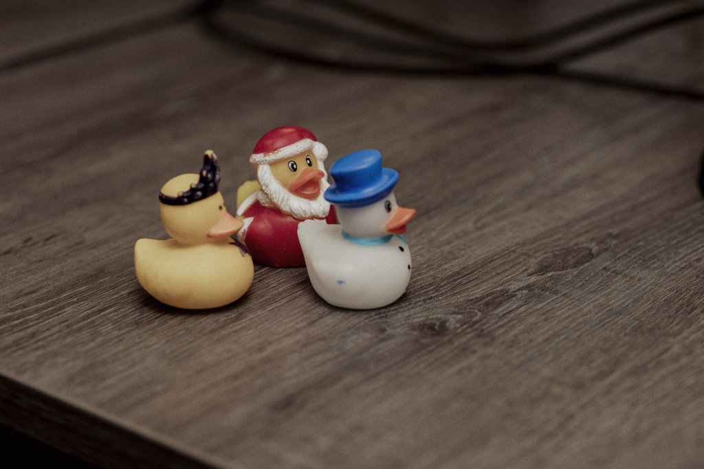 Drie kleine rubberen badeendjes in verschillende kleuren staan op een houten tafel