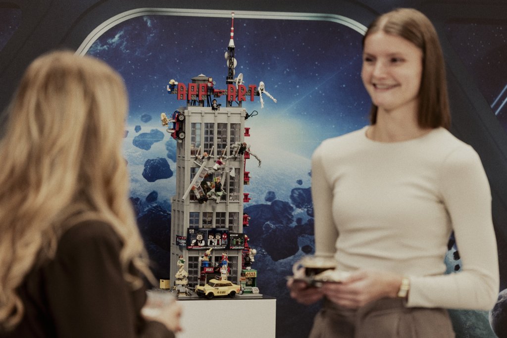 Twee vrouwen staan voor een grote LEGO-toren met “Appart” erop en hebben kort overleg.